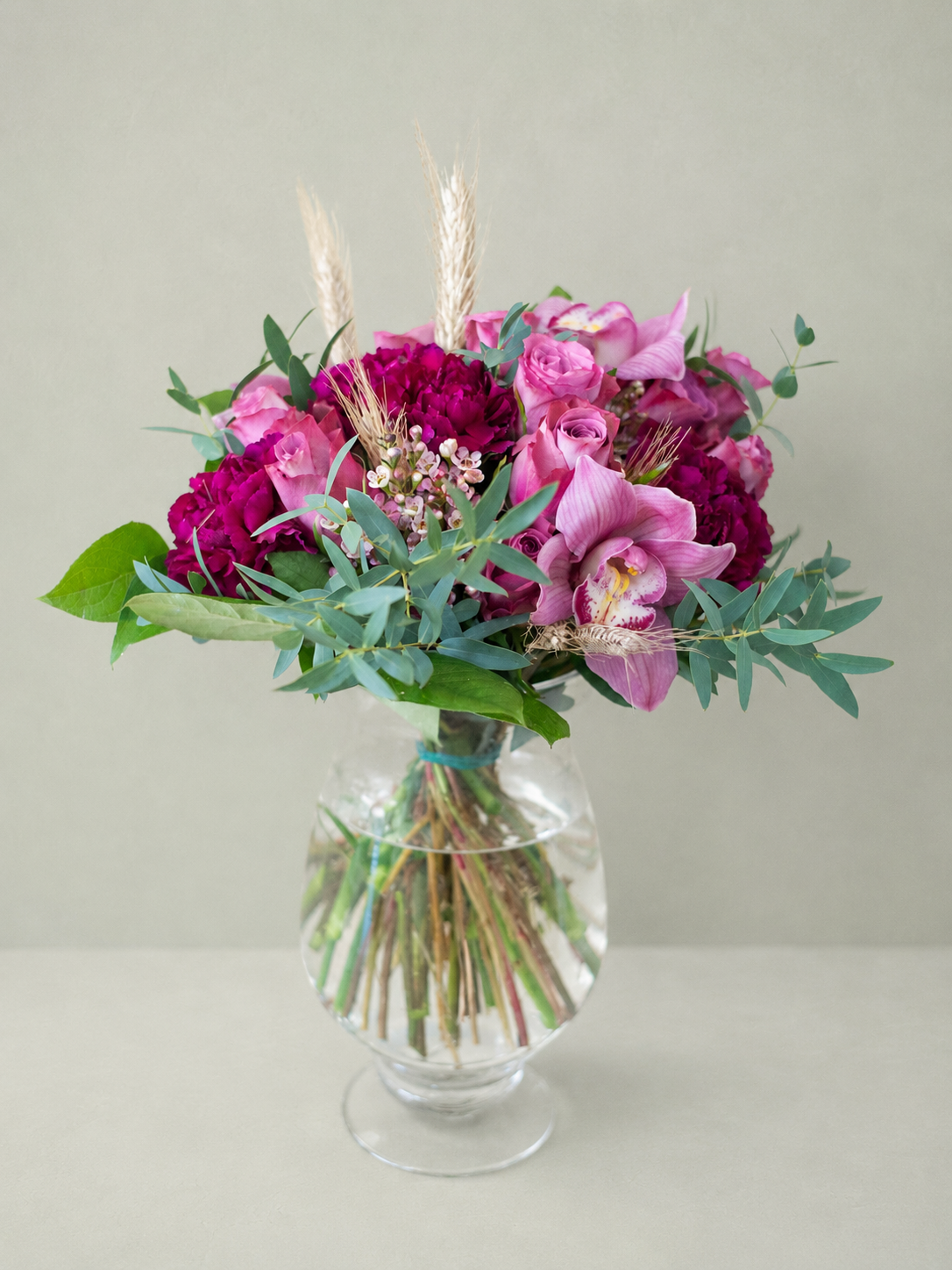 Bouquet of pink and purple flowers in a clear glass vase on a light gray background