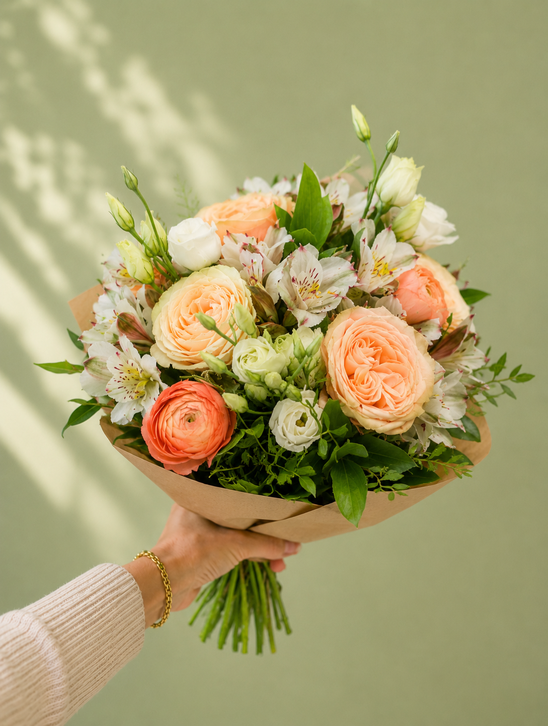 Bouquet of peach and white flowers held by a person against a green background
